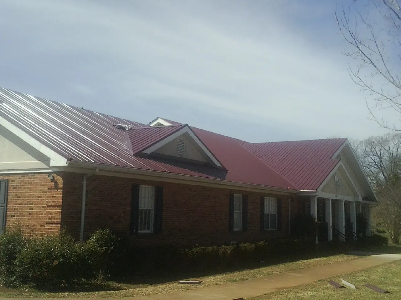 Red metal roof with gabled entries on a long brick building, from a Hail Damage Roof Repair job in Oysterville