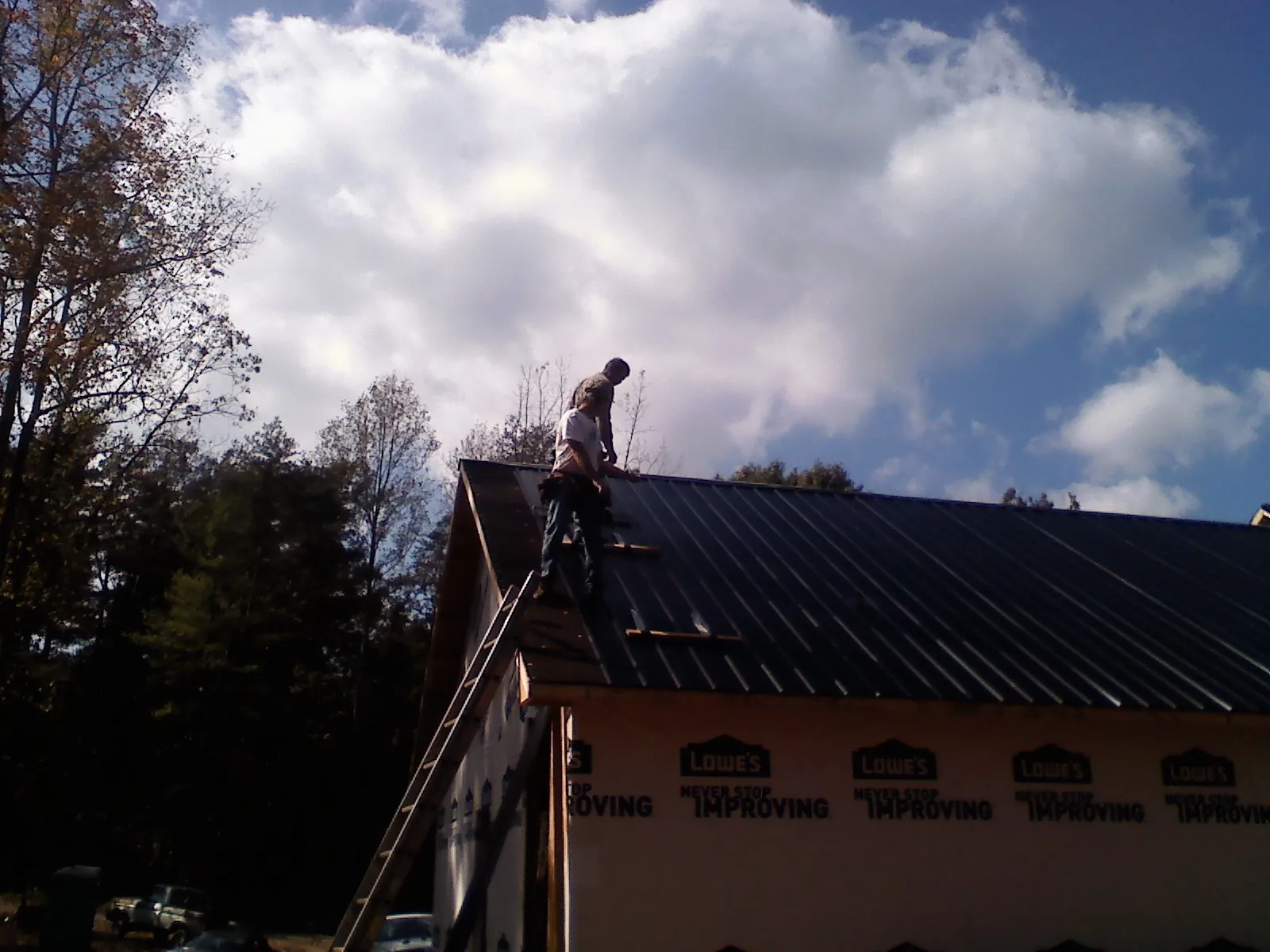 Roofer fastening dark metal panels high against a cloudy sky, from a Roof Inspection job in Oysterville