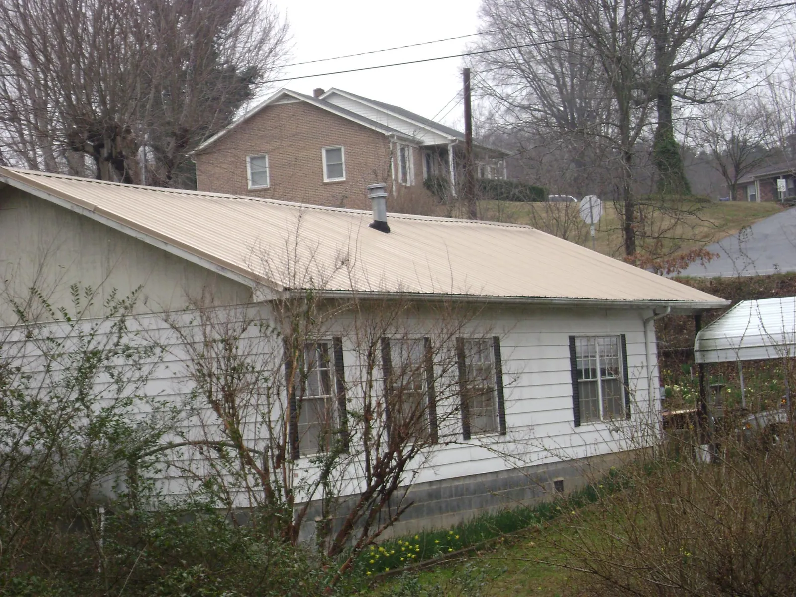 Tan metal roof on a white sided house set into a hillside — Commercial Roofing by Roofing Brothers in Oysterville